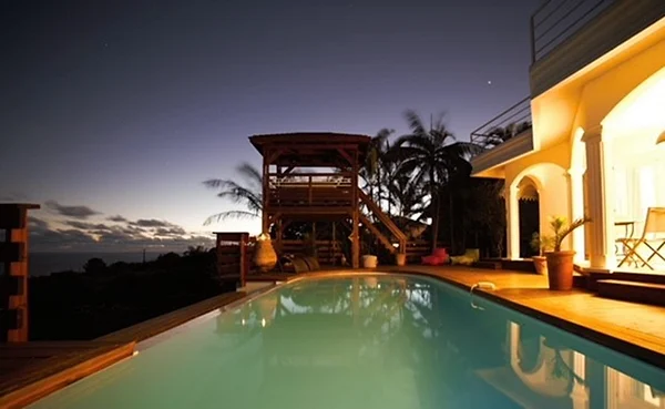 La piscine à débordement à la tombée de la nuit, le kiosque du jacuzzi et la maison éclairée
